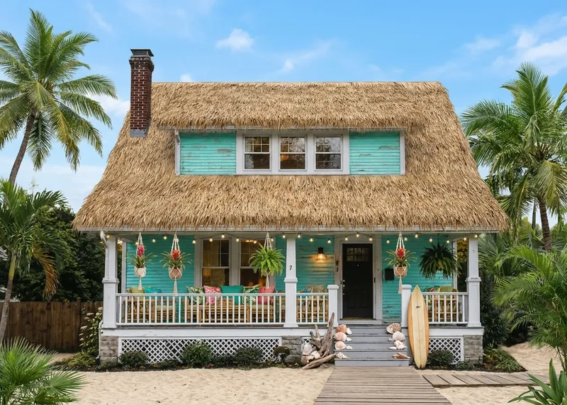 Un cottage de plage turquoise au toit de chaume avec des planches de surf encadrées par des palmiers