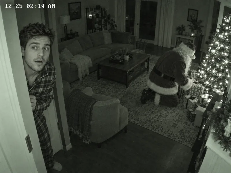 ChatGPT security camera still: the man in plaid pajamas peeking around a doorway at night, surprised, while Santa kneels by a lit tree placing presents, with a 12-25 02:14 AM timestamp in the corner
